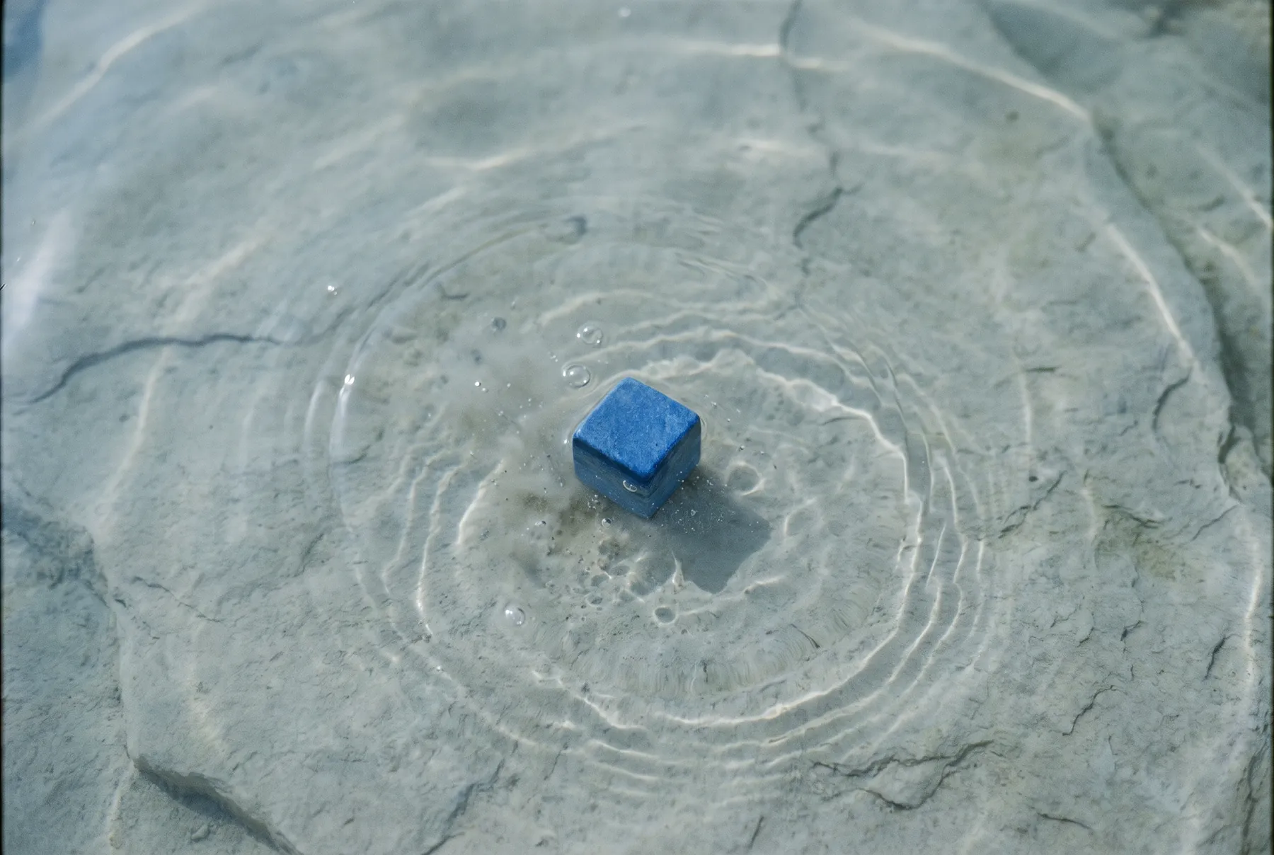 Blauer Würfel in flachem Wasser, Kreise breiten sich aus